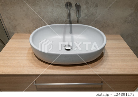 Minimalist bathroom sink with a sleek white basin on a wooden countertop and wall-mounted faucet 124891175