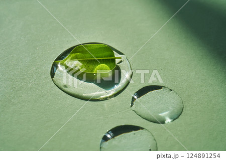 Drop of face serum with green leaf on green background. 124891254
