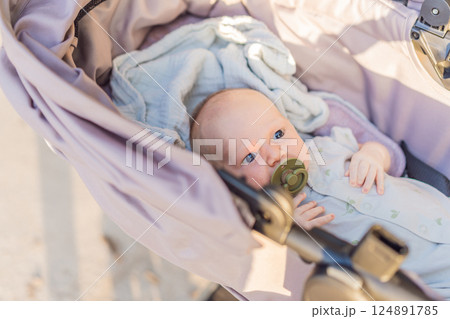 Mother walking with her baby in a stroller in the park. Peaceful outdoor bonding time. Parenthood, baby care, and family lifestyle concept 124891785