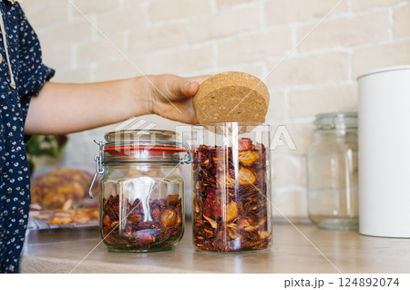 Woman Organizes Dried Fruit in Glass Jars on Kitchen Countertop 124892074