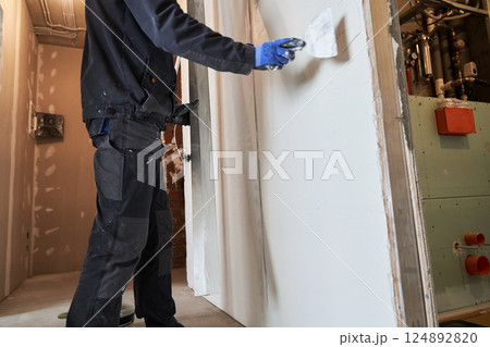 A construction plasterer levels a layer of plaster on a wall using a repair and construction spatula with one hand, holding the rule with the other. Leaving room for copying. High quality photo A construction plasterer levels a layer of plaster on a wall using a repair and construction spatula with one hand, holding the rule with the other. Leaving room for copying. High quality photo 124892820