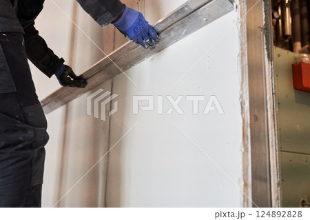 Apartment renovation. Leveling the plastered wall. Home improvement. Men's hands in protective gloves with a building rule. High quality photo 124892828