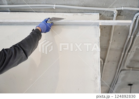 A male plasterer holds a metal rule in his hands and smears plaster on the wall. High quality photo A male plasterer holds a metal rule in his hands and smears plaster on the wall. High quality photo 124892830
