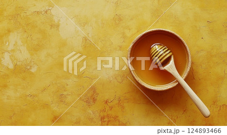 Honey in a bowl with a wooden spoon on a vibrant yellow background 124893466