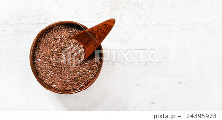 Small wooden bowl full of common flax linseed - Linum usitatissimum - little scoop inside, on white stone like desk, view from above, space for text right side 124895978