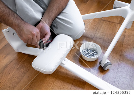 Male adult assembling white office chair with tools and screws on wooden floor Male adult assembling white office chair with tools and screws on wooden floor 124896353