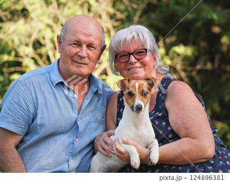 Senior man and woman sitting together with small Jack Russell terrier dog on hands, smiling Senior man and woman sitting together with small Jack Russell terrier dog on hands, smiling 124896381