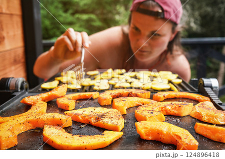 Butternut squash pieces grilled on electric grill, focus on bright orange vegetables seasoned with spice, blurred young woman in background Butternut squash pieces grilled on electric grill, focus on bright orange vegetables seasoned with spice, blurred young woman in background 124896418