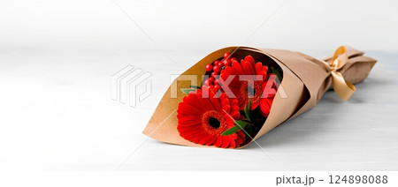 Red gerbera flowers bouquet wrapped in paper on a light background 124898088