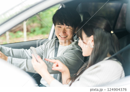 車内でスマホを見ながら会話する若いアジア人カップル,夫婦 124904376