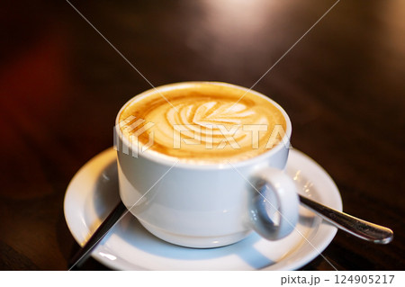 A cup of cappuccino on a saucer with a spoon 124905217