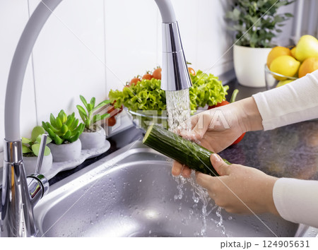 Woman hands washing a cucumber to prepare a fresh salad in the kitchen Woman hands washing a cucumber to prepare a fresh salad in the kitchen 124905631