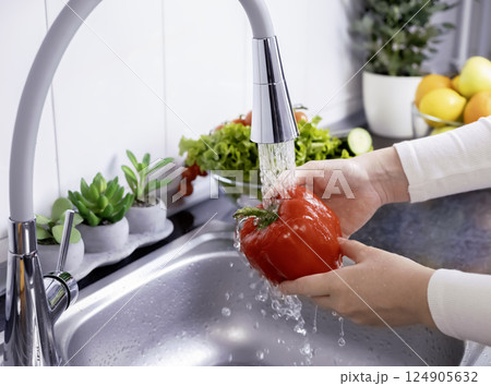 Woman hands washing a red bell pepper to prepare a fresh salad in the kitchen Woman hands washing a red bell pepper to prepare a fresh salad in the kitchen 124905632