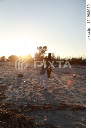 Girl Walks And Plays The Bass Instrument On The Beach Near The Ocean At Sunset Girl Walks And Plays The Bass Instrument On The Beach Near The Ocean At Sunset 124908050