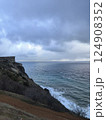 Cliffside landscape with rocky terrain leading to vast ocean under a cloudy sky. Vegetation covers the slope, merging with waves below. The scene evokes tranquility and nature's splendor Cliffside landscape with rocky terrain leading to vast ocean under a cloudy sky. Vegetation covers the slope, merging with waves below. The scene evokes tranquility and nature's splendor 124908352