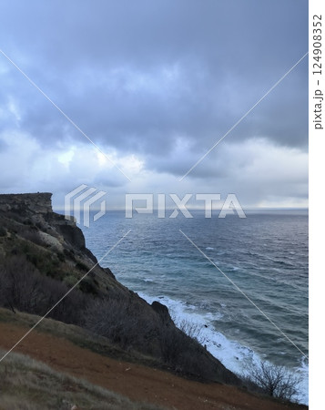 Cliffside landscape with rocky terrain leading to vast ocean under a cloudy sky. Vegetation covers the slope, merging with waves below. The scene evokes tranquility and nature's splendor Cliffside landscape with rocky terrain leading to vast ocean under a cloudy sky. Vegetation covers the slope, merging with waves below. The scene evokes tranquility and nature's splendor 124908352