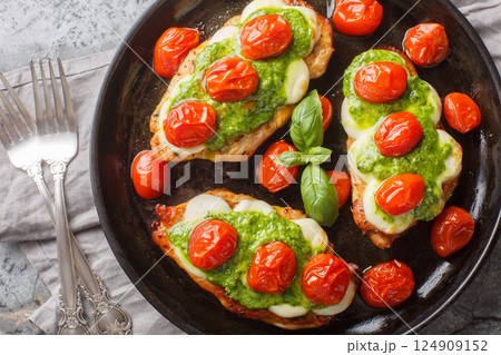 Roasted Margherita chicken breasts topped with melted mozzarella, pesto and cherry tomatoes close-up on pan. Horizontal top view 124909152