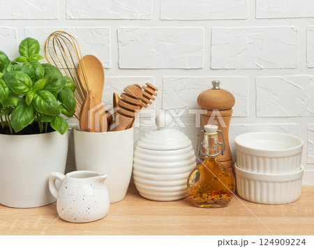Kitchen utensils, basil plant and condiments resting on wooden countertop Kitchen utensils, basil plant and condiments resting on wooden countertop 124909224