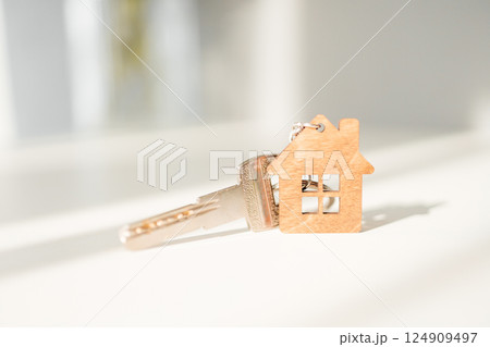 A house key with a keychain in the form of a wooden house on a light background 124909497