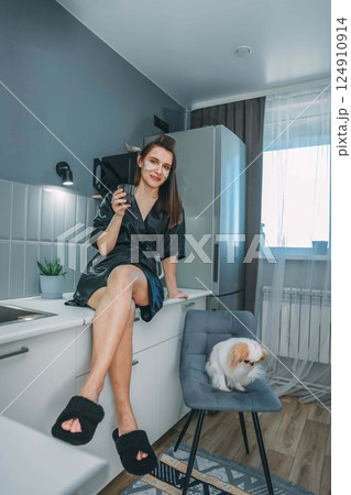 relaxed woman enjoying a glass of water in a modern kitchen, with small dog, concept of daily hydration, vertical relaxed woman enjoying a glass of water in a modern kitchen, with small dog, concept of daily hydration, vertical 124910914