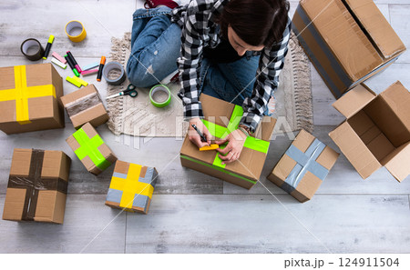 Girl Packs Cardboard Boxes And Seals Them With Tape At Home As She Prepares Them For Delivery Girl Packs Cardboard Boxes And Seals Them With Tape At Home As She Prepares Them For Delivery 124911504