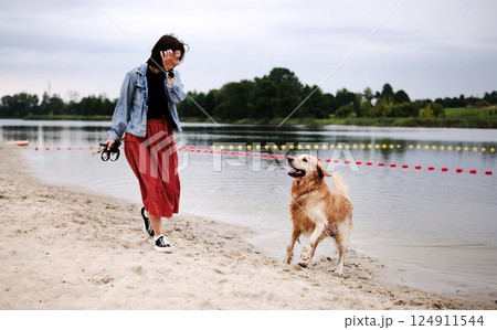 Playful Golden Retriever Runs And Plays With Its Female Owner On The Beach, Enjoying The Outdoors 124911544