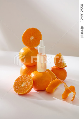 Vertical photo of transparent serum dropper bottles placed on ripe citrus. Three oranges are stacked high and others cut into different shapes. Orange peels are thinly sliced to spiraled. Vertical photo of transparent serum dropper bottles placed on ripe citrus. Three oranges are stacked high and others cut into different shapes. Orange peels are thinly sliced to spiraled. 124912558