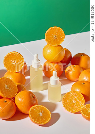 Many oranges are placed randomly around two dropper bottles of serum. Essence extracted from fresh oranges has many benefits in beauty and skincare. The shadows of oranges fall on the table 124912586