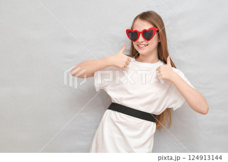 Caucasian young girl with heart-shaped sunglasses giving thumbs up in casual 124913144