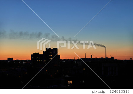 City skyline and factory at sunset with smoke plume against colorful evening sky 124913513