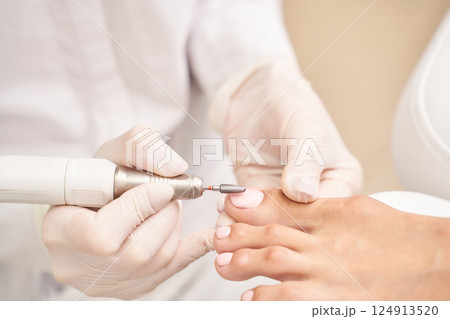 Professional pedicure treatment on female feet with machine tool by gloved Professional pedicure treatment on female feet with machine tool by gloved 124913520