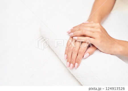 Female hands with neutral nail polish resting on white towel with clean 124913526