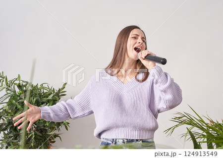 A woman in a purple sweater is singing passionately into a mic 124913549