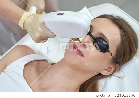 Young caucasian female receiving laser facial treatment in spa clinic 124913576