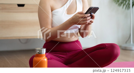 Hydration and Self-Care. A woman checking her phone after a yoga session, highlighting the importance of hydration and wellness. 124917315
