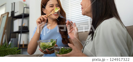 Healthy Eating and Connection. A cheerful daughter feeding her mother salad in a warm home setting. Healthy Eating and Connection. A cheerful daughter feeding her mother salad in a warm home setting. 124917322