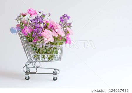 Shopping cart with summer pink flowers on white background, an empty space for text. Festive banner, template for advertisements of online shopping, flower delivery, weddings, floral gifts 124917455