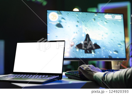 Isolated screen laptop next to man playing with friends online, shooting asteroids together in spaceship flying game. Mockup notebook next to gamer cooperating with teammates in coop videogame 124920393