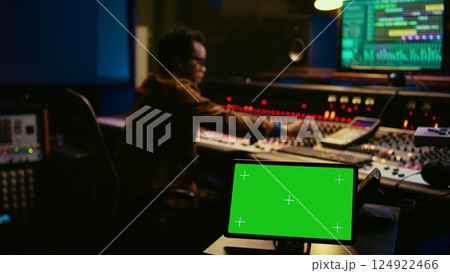 African american tracking engineer works with greenscreen, operates audio console with moving faders and colored meters. Specialist pressing buttons and faders to edit audio recordings. Camera B. 124922466