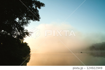 Landscape with a silhouette of a boat on a lake covered with fog at dawn 124922949