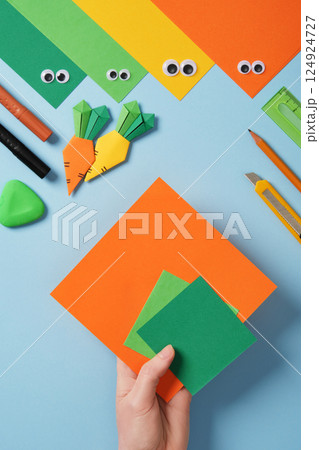 Making origami carrot. DIY project. Take a square sheet of orange color and two small squares of green color. Making origami carrot. DIY project. Take a square sheet of orange color and two small squares of green color. 124924727