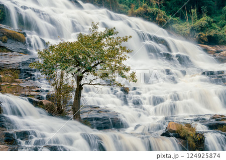 Beautiful waterfall with a lush green forest in the background. The water is flowing down the rocks and creating a beautiful scene. Sustainable waterfall in lush forest promoting water sustainability. Beautiful waterfall with a lush green forest in the background. The water is flowing down the rocks and creating a beautiful scene. Sustainable waterfall in lush forest promoting water sustainability. 124925874