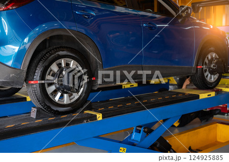 Wheel alignment equipment grip the tire of car wheel in car repair shop. Auto wheel alignment in workshop of service station. Car wheel balance. Suspension adjustment. Vehicle inside garage workshop. 124925885