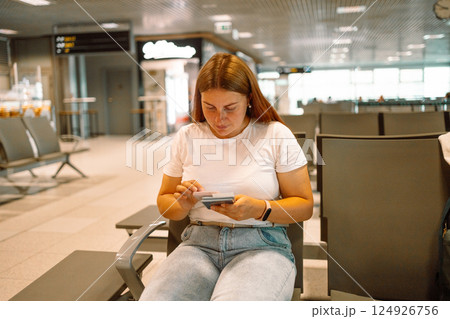 Women use smartphone and holding a passport while waiting to board a flight at the airport Women use smartphone and holding a passport while waiting to board a flight at the airport 124926756