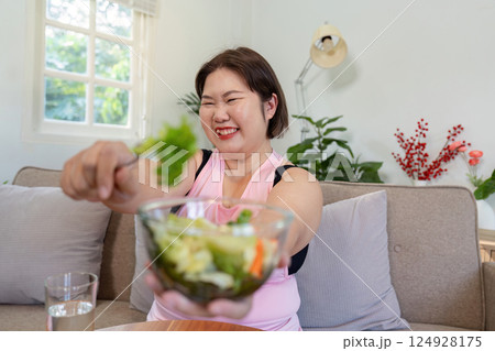 Enthusiastic overweight woman sharing a vibrant salad, celebrating her commitment to weight loss and healthy living 124928175