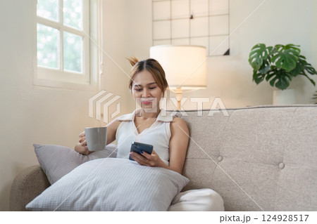 Relaxing woman enjoys coffee while using smartphone at home living room cozy environment casual lifestyle 124928517