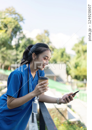 Nurse engaging with smartphone while enjoying coffee outdoor setting lifestyle image nature background positive vibes Nurse engaging with smartphone while enjoying coffee outdoor setting lifestyle image nature background positive vibes 124928607