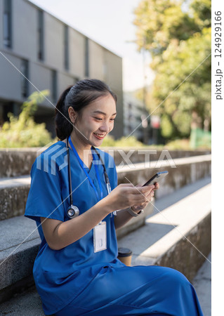 Asian nurse texting outdoors in blue scrubs Asian nurse texting outdoors in blue scrubs 124929166