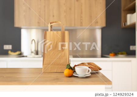 Paper shopping bag and fresh citrus, cup of coffee and sandwich on countertop in kitchen. Space for text. Delivery concept, mock up 124929324