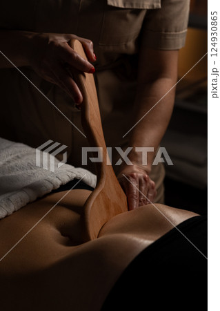 Anti-cellulite massage on the stomach using wooden objects. Massage salon in a dark room. 124930865